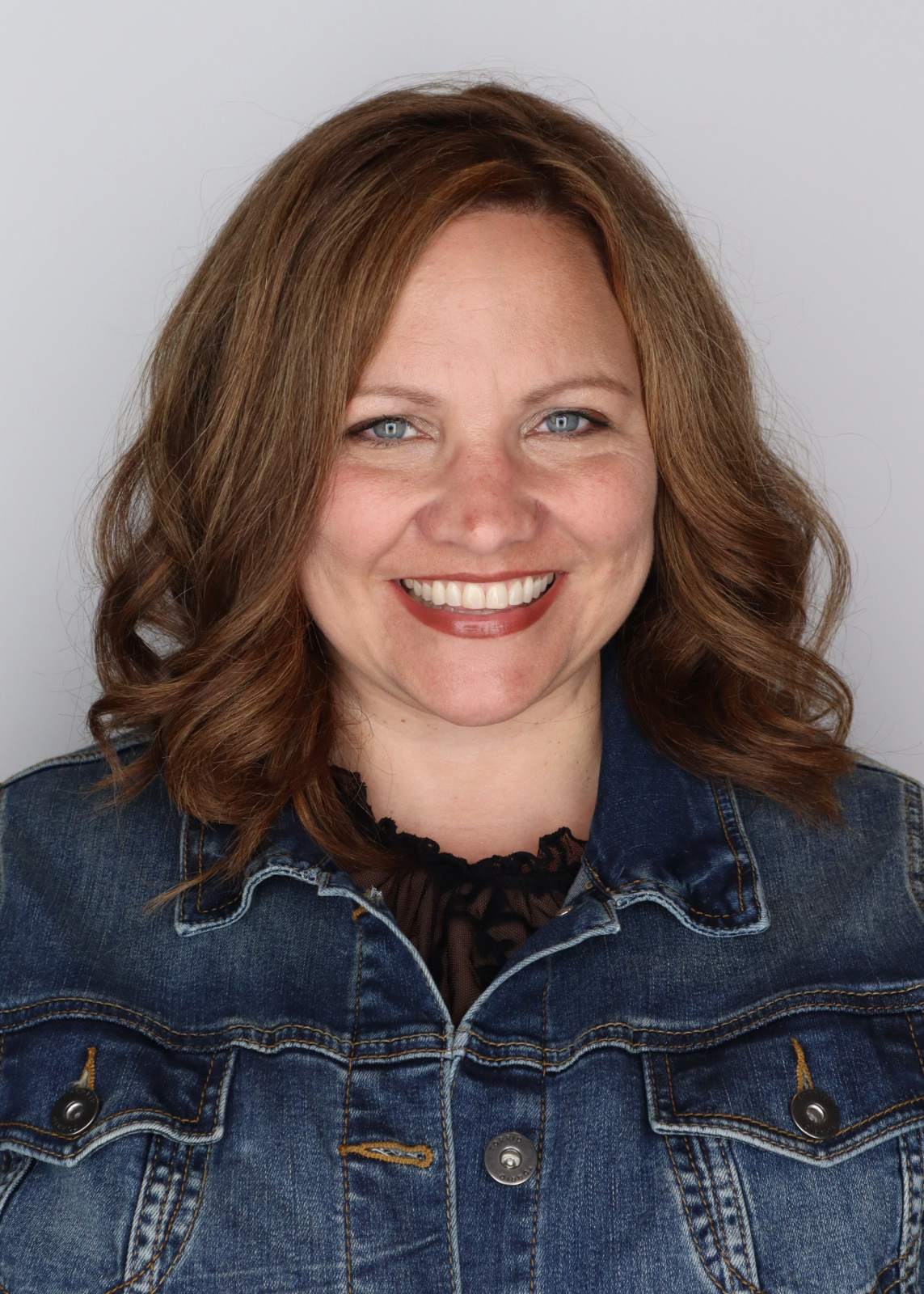 Headshot of a light-skinned woman wearing a jean jacket on a gray background